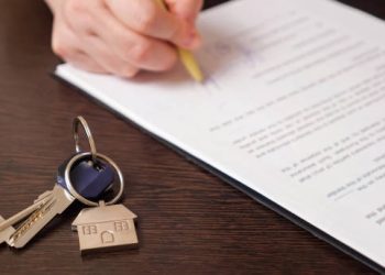 Man client signs new apartment purchase contract with pen near keys with house shaped breloque put on table extreme close view
